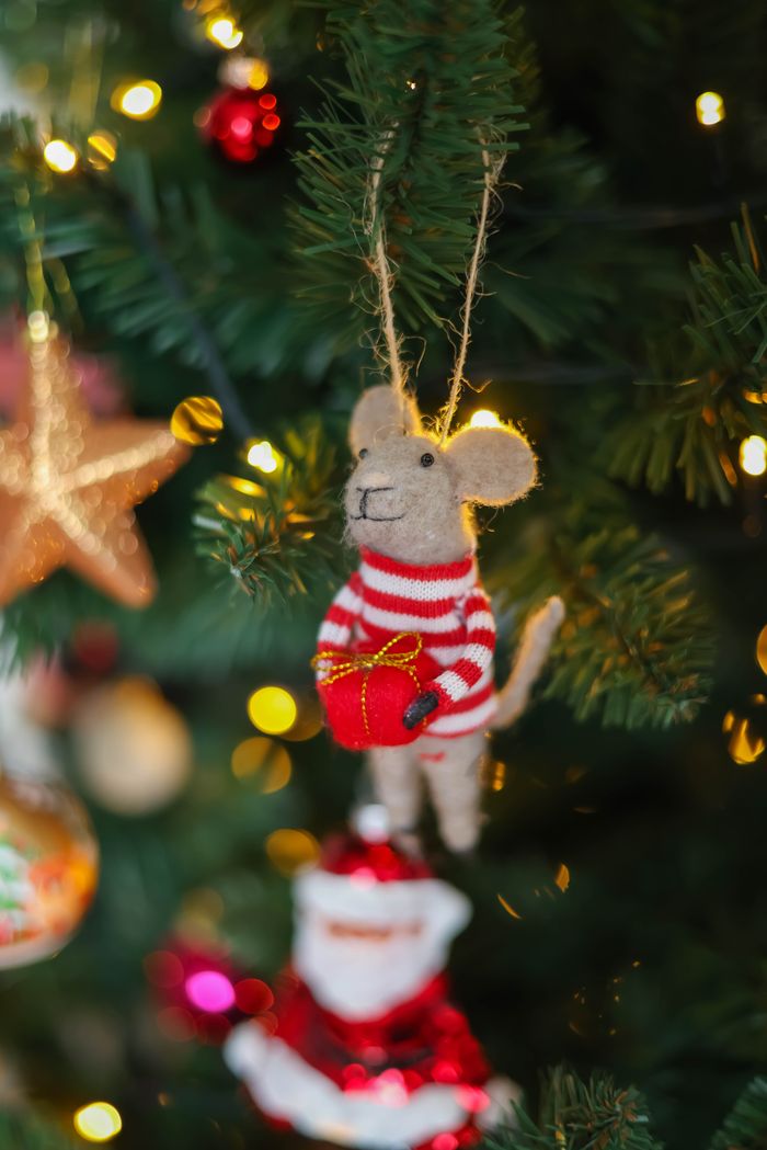 Close-up of a cute mouse ornament hanging on a decorated Christmas tree with lights.