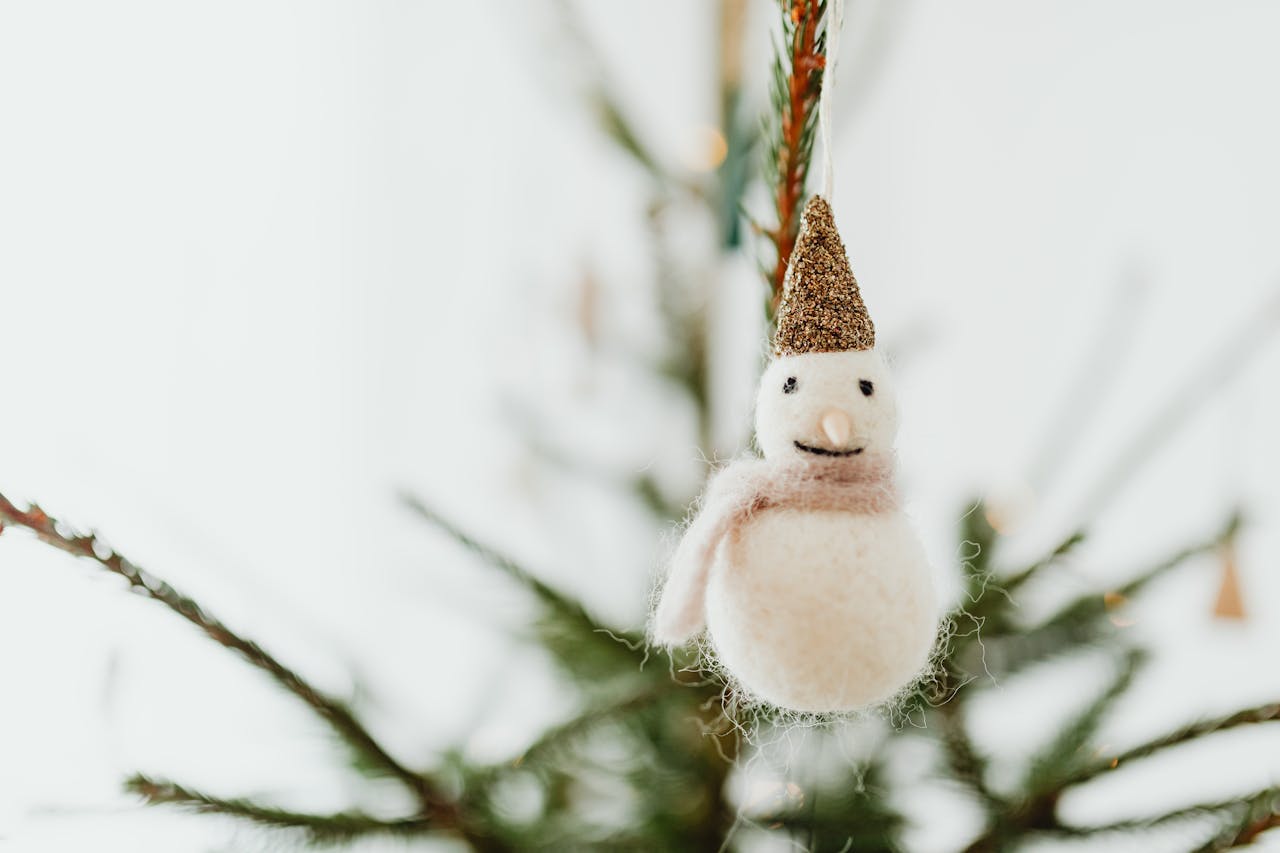 Close-up of a soft snowman ornament hanging on a festive Christmas tree branch.